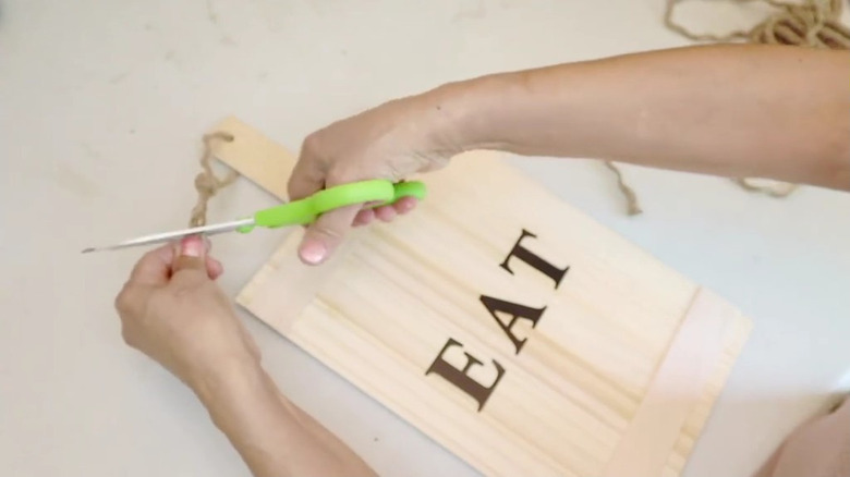 A crafter creates a decorative sign in a cutting board shape with wooden rulers