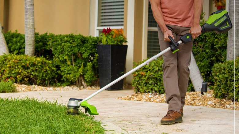 Person using Greenworks 60V Cordless String Trimmer to cut lawn around pathway