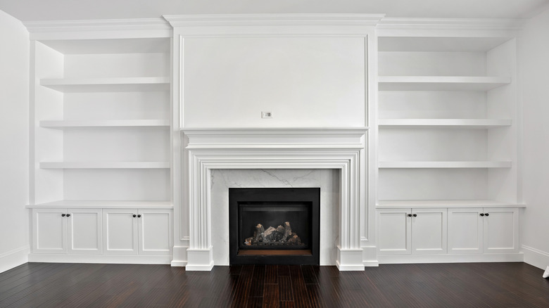 A wooden fireplace mantle with built-in bookcases on each side, all painted white
