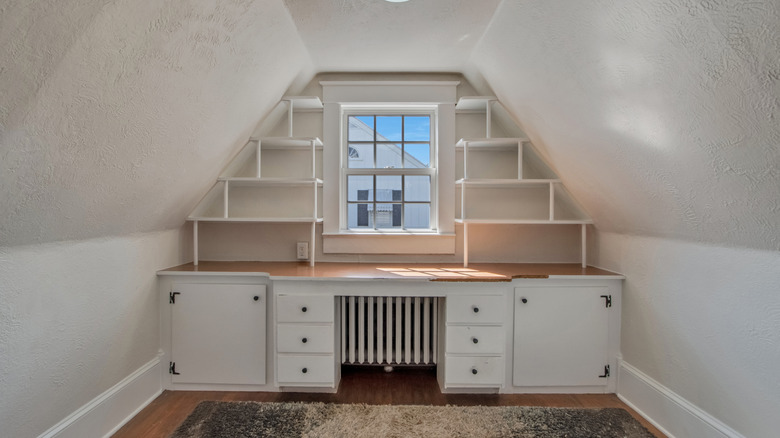 An attic in an older home with built-in cabinets and shelves around a radiator