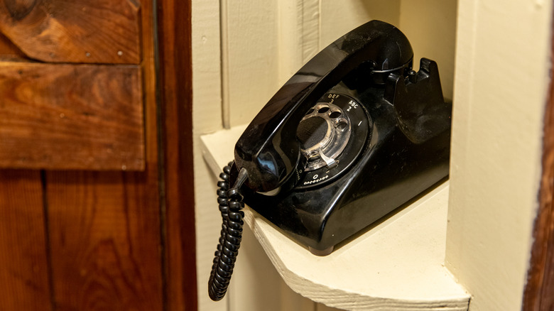A black rotary phone off the hook in a phone nook