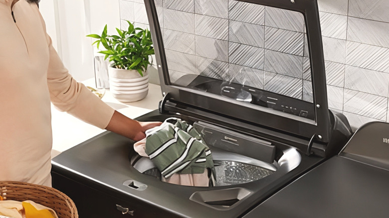 a person putting clothes in the Whirlpool top-load washer