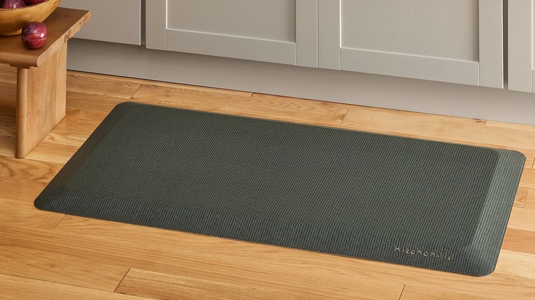 A forest green gel mat lays on a wooden kitchen floor