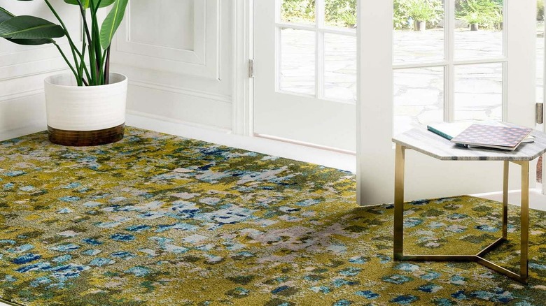 A geometric side table and potted plant sit on a green entryway rug