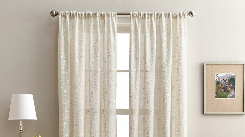 A table lamp and framed photo flank a window covered in sheer window curtains