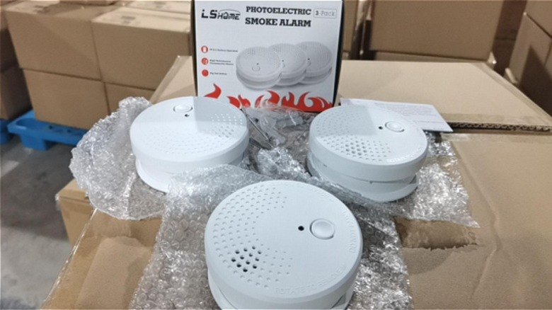 Three unpackaged white fire alarm units sitting on top of cardboard boxes.