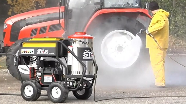 A man in yellow clothing power washing a tractor with a NorthStar hot water pressure washer.