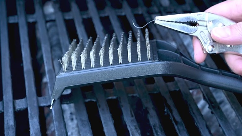 Hand holding pliers to show a metal wire bristle that has fallen out of a grill brush.