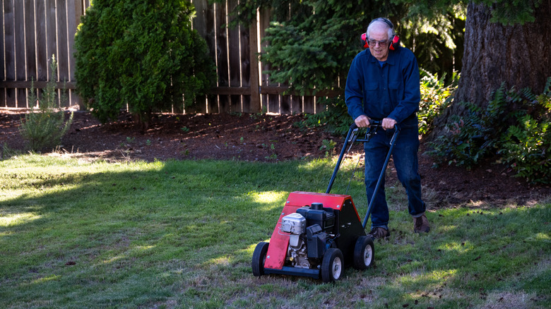 A man using a garden aerating machine on his lawn