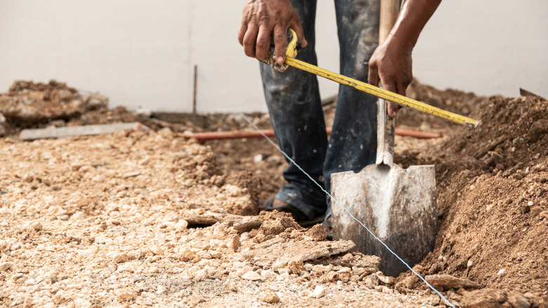 A man measuring dug foundations in a garden