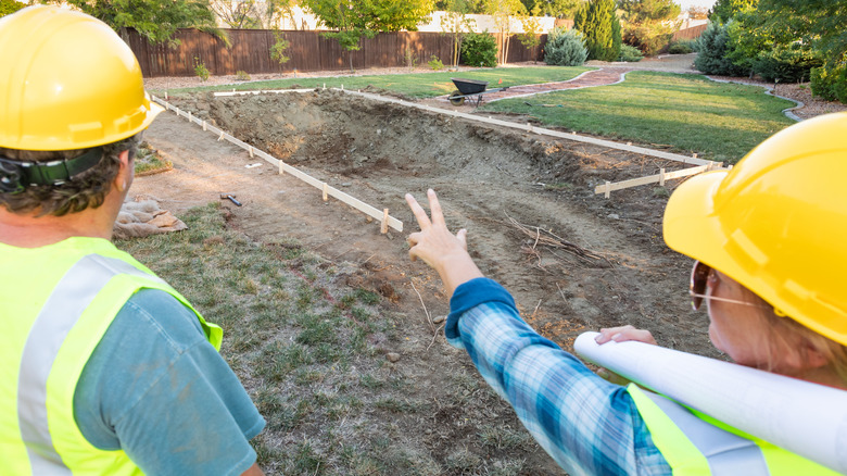 A man and woman wearing hardhats examining a garden swimming pool construction site