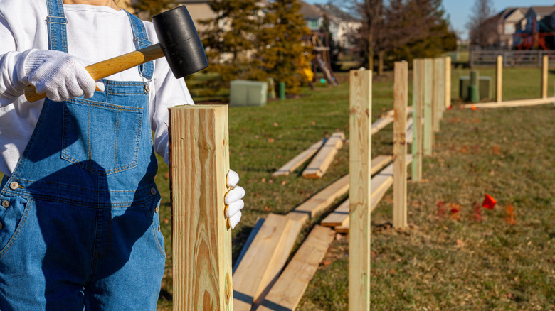 A woman using a mallet to hammer fence posts in place