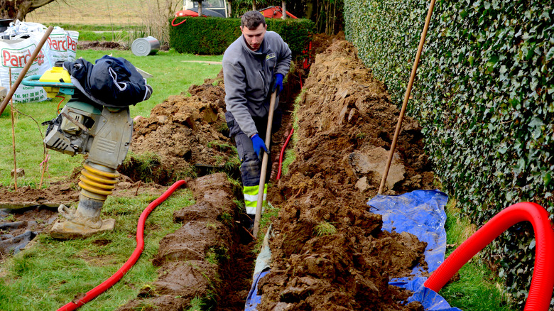 A worker in a garden laying pipework in a trench for electrical cables