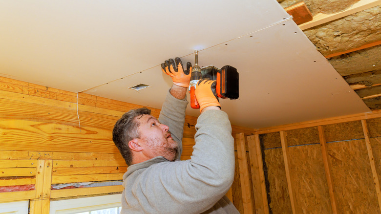 Man installing drywall over a basement ceiling