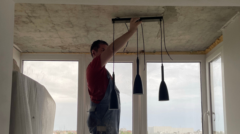 Man holding a new pendant light fixture to a ceiling