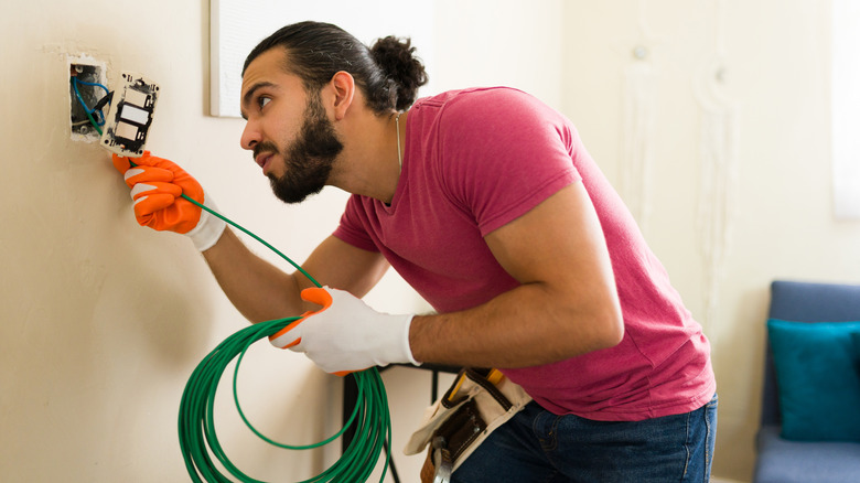 Man looking at a switch outlet and holding a roll of green wire