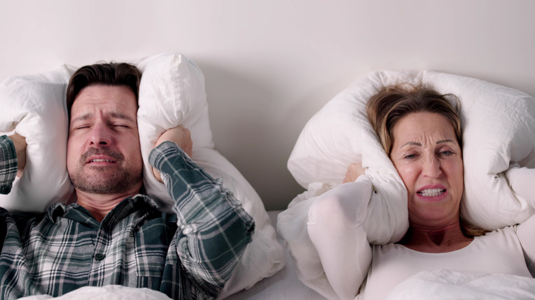 A couple in bed holding pillows over their ears