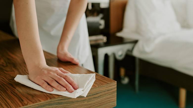 A woman wiping a wooden table with a white towel