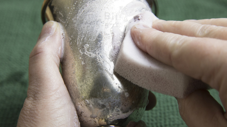 Close up of woman's hands using sponge to polish tarnish off silver goblet