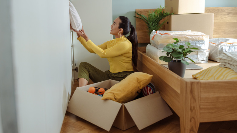 A woman sorts and organizes belongings in a bedroom surrounded by boxes and linen