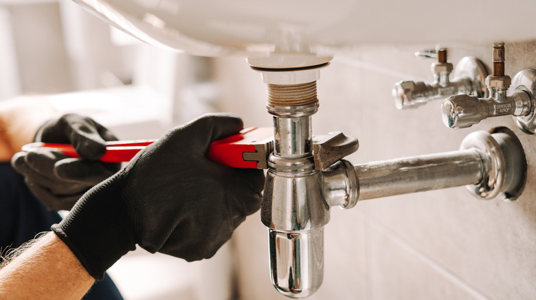 Close-up of a person with black gloves fixing a leaky pipe