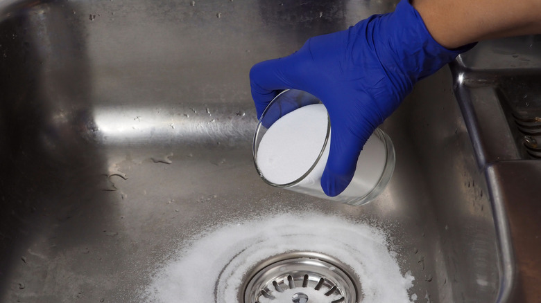 A gloved hand pouring baking soda into a drain