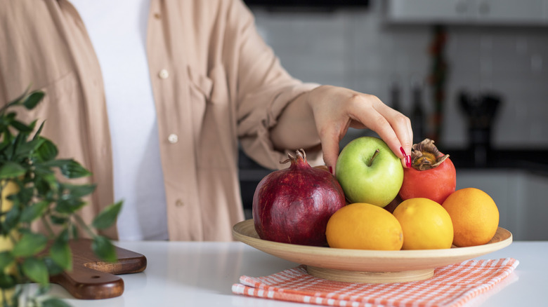 A person grabbing an apple from a fruit bowl