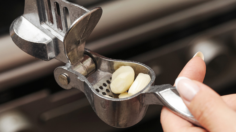 Hands holding a garlic press with cloves of garlic in it