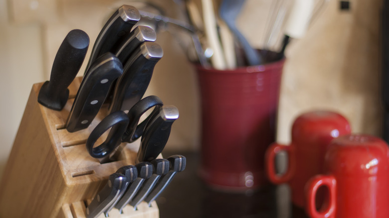 Knife block on a kitchen counter next to mugs and a vase.