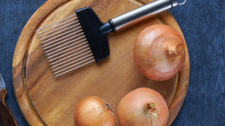 An onion holder on a cutting board with three onion bulbs