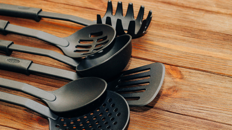 Black plastic cooking utensils on a wooden table.