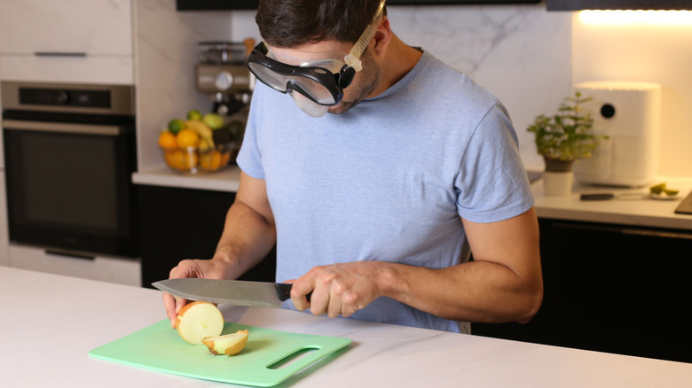 Man slicing onions on a cutting board while wearing goggles