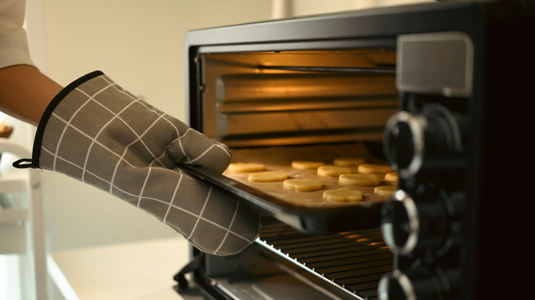 Home cook sliding cookies into the oven with a grey and white checkered oven mitt
