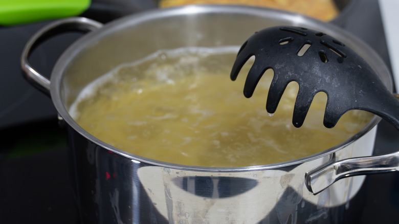 A pasta spoon next to a poiling pot of pasta