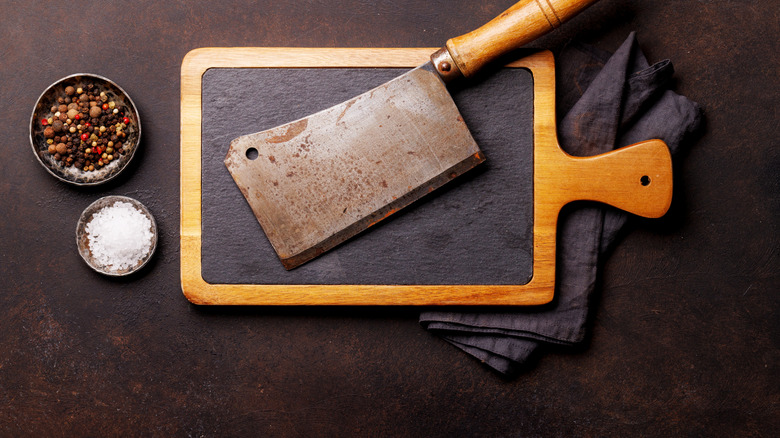 A large, roughed-up knife on top of a stone cutting board in wooden frame