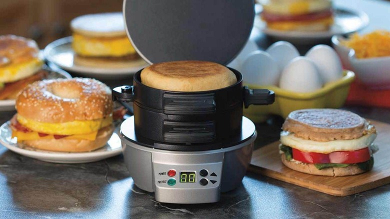 An open breakfast sandwich maker with various sandwiches in the background