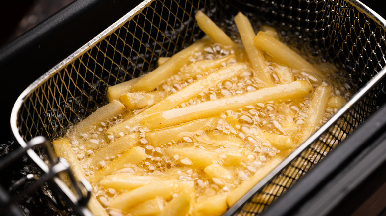 A deep fryer with a basket with fries inside hot oil