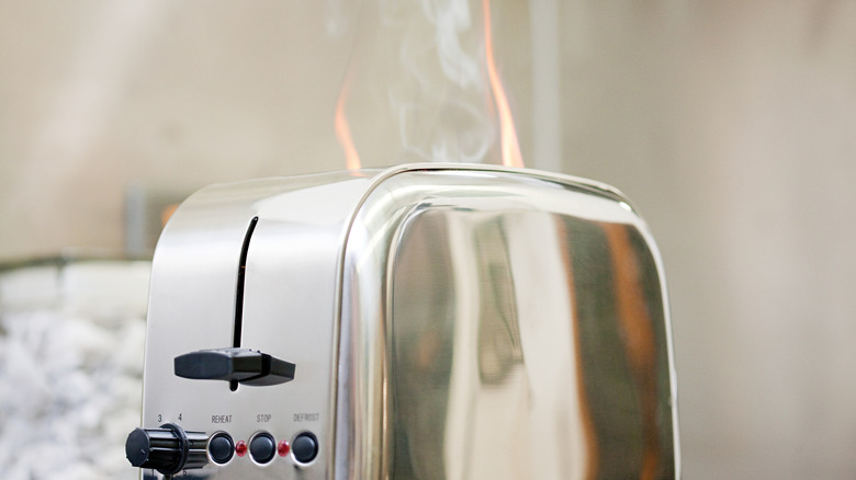 A silver toaster with flames and smoke coming out of the top
