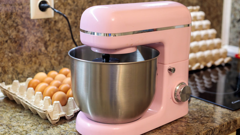 A bright pink stand mixer on a kitchen counter by the stove with a large carton of eggs behind