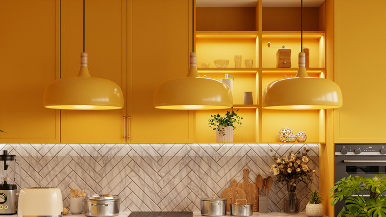 A modern yellow kitchen with hanging overhead lamps and a variety of kitchen utensils on the sideboards