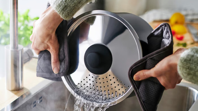 Someone holding an IKEA pot lid with pot holders and straining water into the sink