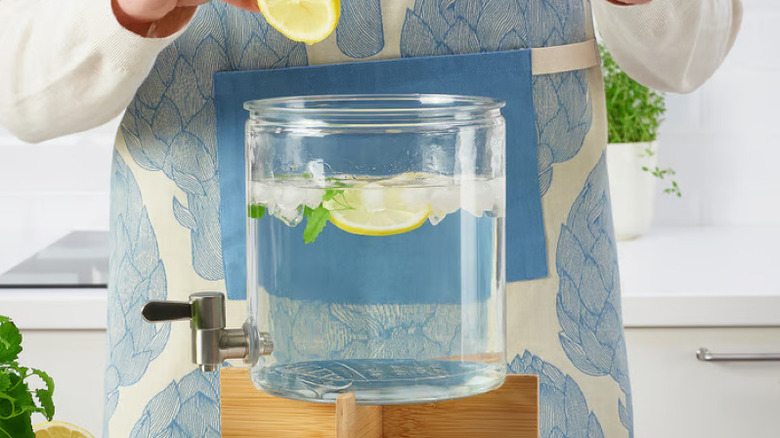Someone filling an IKEA beverage dispenser with water, ice, lemon, and leaves