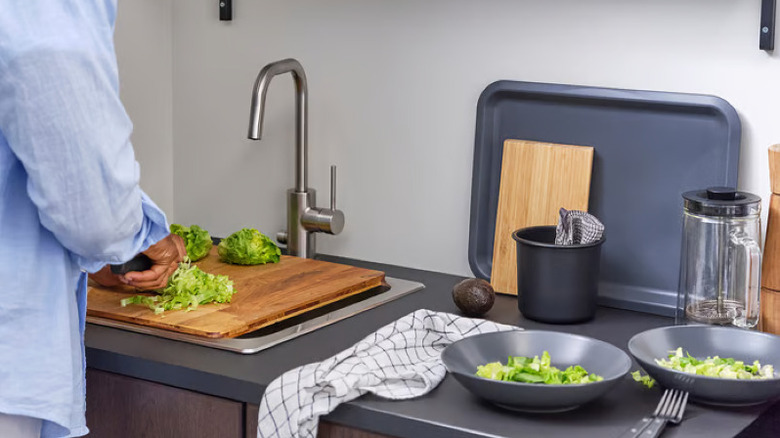 Someone preparing rinsed lettuce on wood cutting board over a sink.