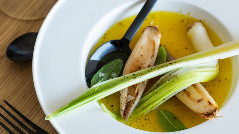An IKEA deep dish plate filled with a vegetable and oil dish with a black spoon on the side