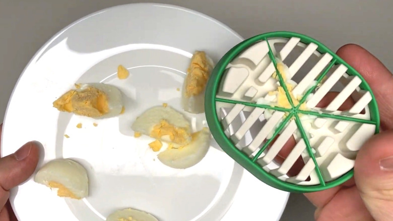 Someone holding a green IKEA egg slicer over squashed hard-boiled eggs on white plate