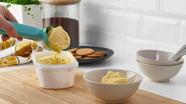 Someone scooping sticky ice cream from a tub into a bowl with a blue IKEA ice cream scoop