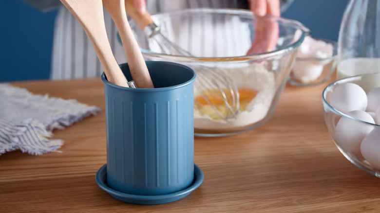 A Blue IKEA utensil holder holding wooden utensils while someone whisks baking ingredients in the background