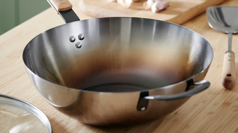 A hot carbon steel IKEA wok with a browned center on a wood table a with lid and spatula nearby