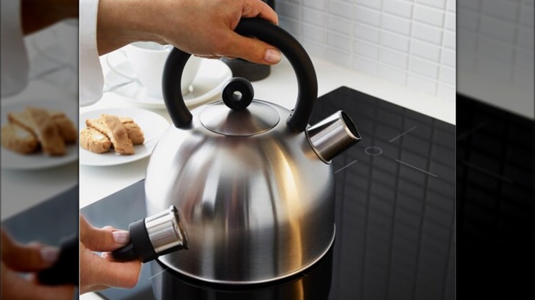 Someone putting a stainless steel IKEA kettle on an electric stovetop