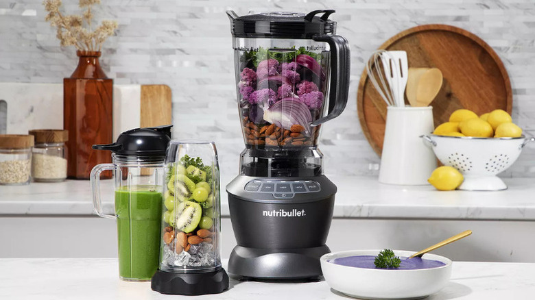 A NutriBullet blender next to two plastic cups filled with smoothie and fruit